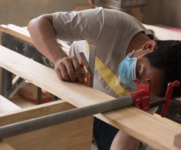 A shallow focus of a Southeast Asian carpenter working on polished wood planks in the workshop