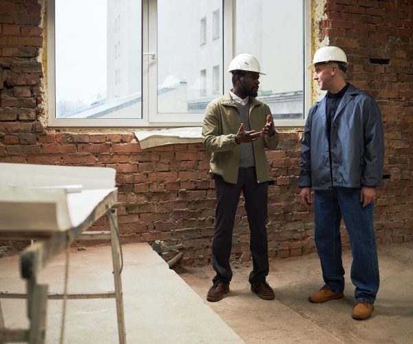 Two biracial builders having conversation while working at construction site together